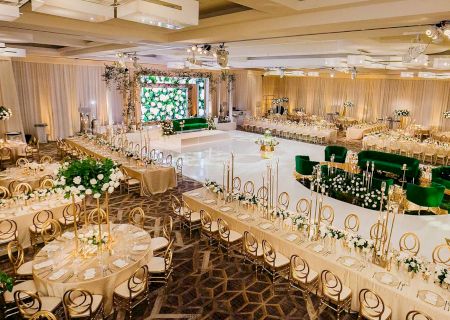 The image shows an elegant banquet hall with round tables, floral arrangements, gold chairs, and a central dance floor.