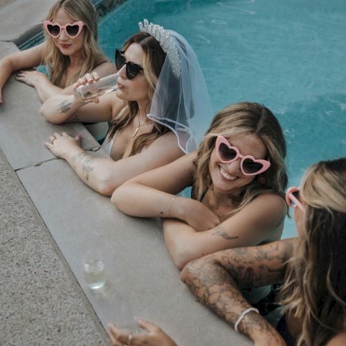 Four people are in a pool wearing sunglasses; one has a bridal veil, suggesting a bachelorette party theme, with drinks nearby.