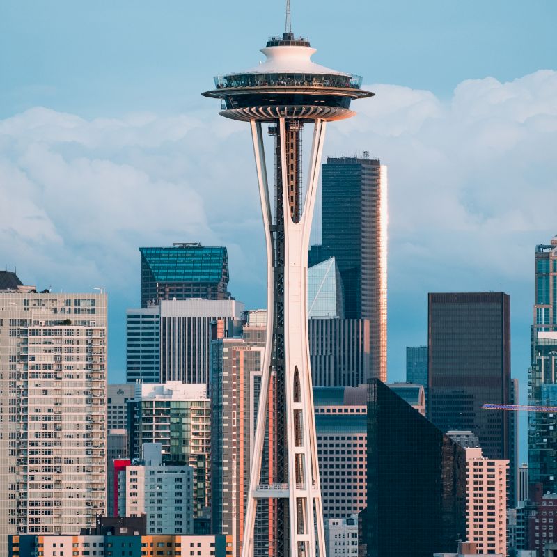 The image shows the Seattle skyline with the prominent Space Needle, surrounded by modern skyscrapers under a partly cloudy sky.