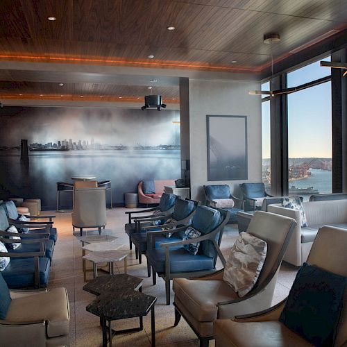 A modern lounge with comfortable seating, large windows offering a scenic view, and a city skyline mural on the wall.