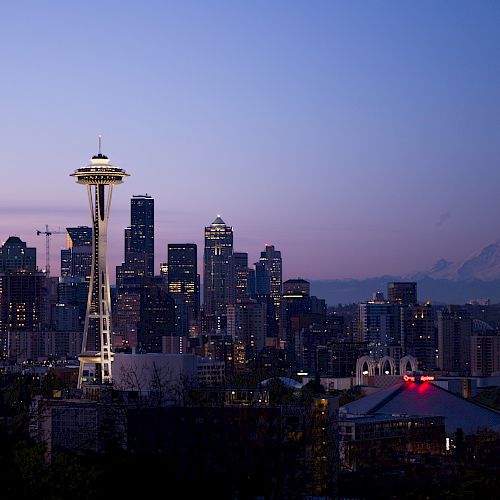 Seattle skyline at dusk featuring the Space Needle, surrounding city buildings, and Mount Rainier visible in the distance.