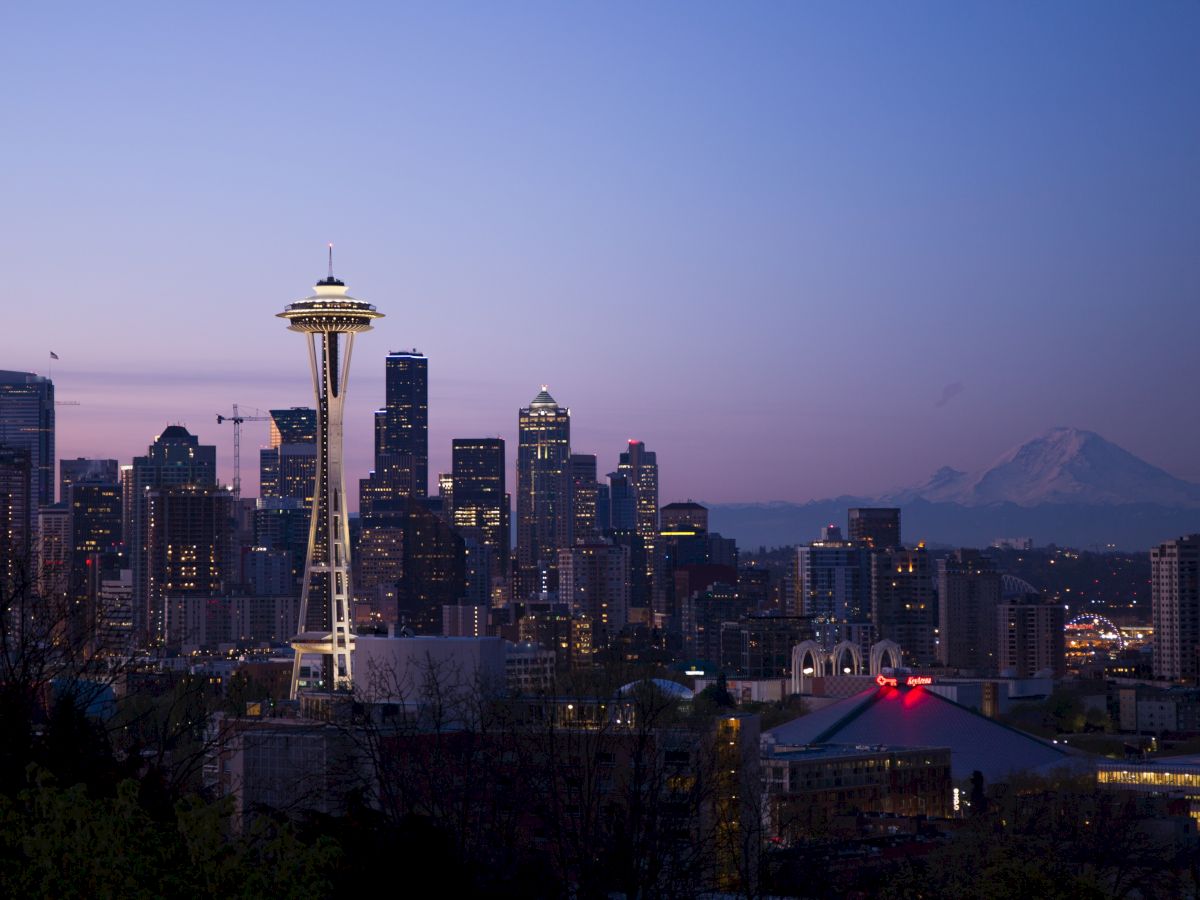 Seattle skyline at dusk with the Space Needle prominently visible and a mountain in the background.
