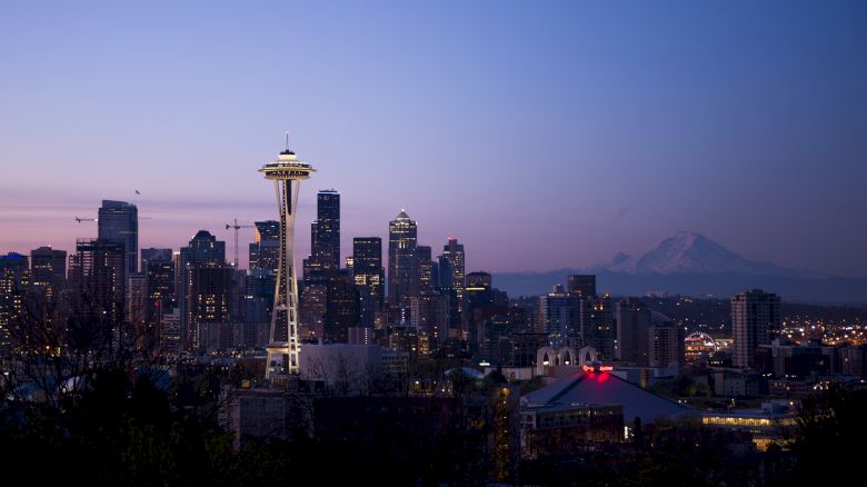 Seattle skyline at dusk with the Space Needle prominently visible and a mountain in the background.