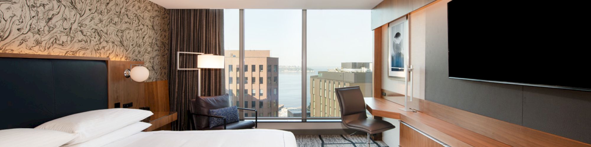 A modern hotel room with a large bed, TV, desk, and a city view through a large window completes the stylish space.